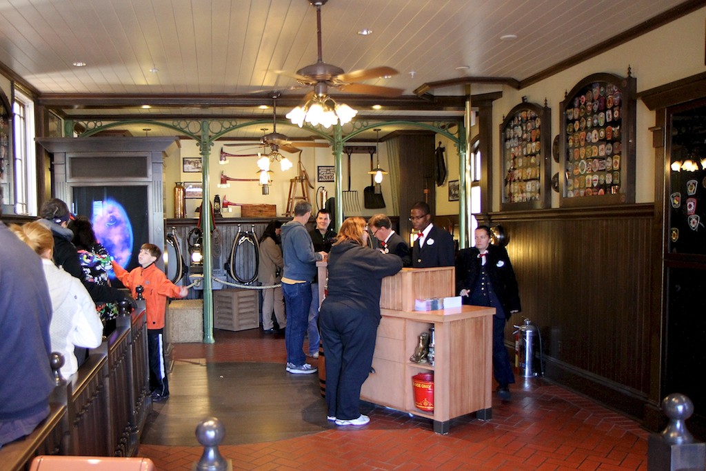 Sorcerers of the Magic Kingdom - Inside the Fire House, a queue runs on the left side, with the signup desks on the right, and a training area at the back of the room
